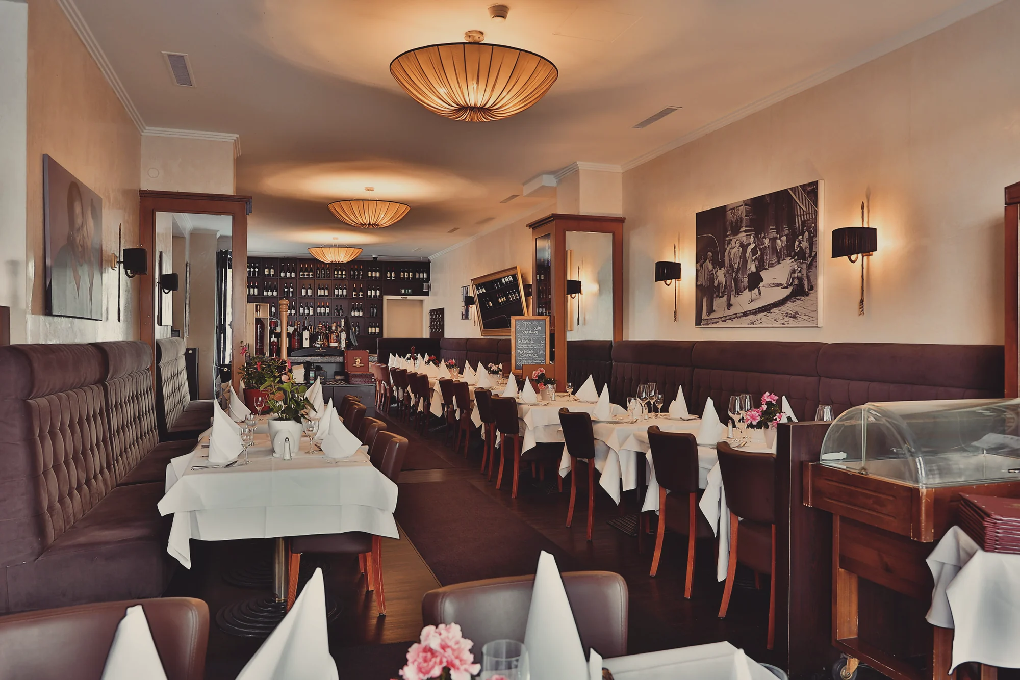 Langer Gastraum des Ristorante Arlecchino mit warmem Licht und weiss gedeckten Tischen